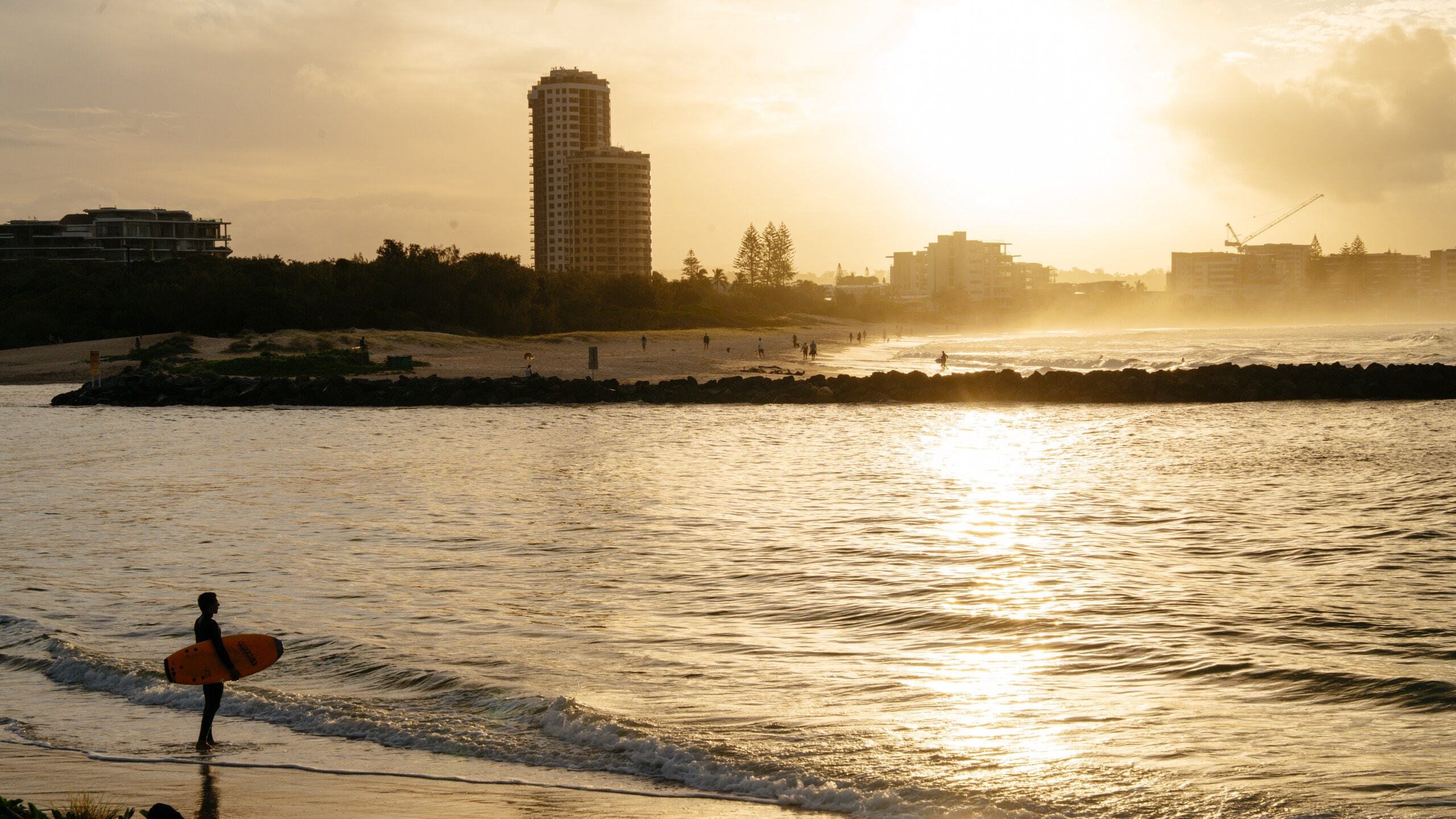A surfer at the creek mouth at sunset, Gold Coast towers in golden light